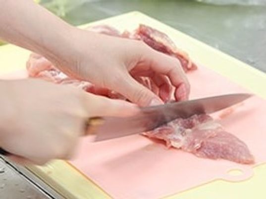 肉の筋を丁寧に取り除いている様子。清潔なまな板と包丁が使われている。