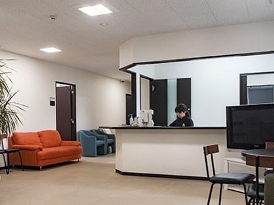 女性スタッフが常駐するスタッフステーション。周辺にはソファやテレビ、テーブルセットが置かれている。