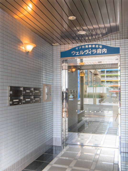 マンションのような雰囲気の建物の入り口付近。ウェルヴィラ府内の看板がある様子