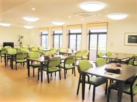 四人掛けのテーブルと椅子が複数組並んでいる施設内の食堂・共有スペースの様子
