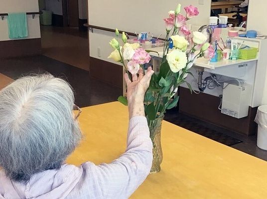 施設内に活けてある花にふれている高齢者の様子。花瓶に生けてある花と施設内の雰囲気