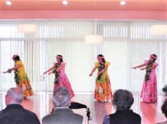 フラダンスをしている女性4名はピンクや黄色のドレスに身を包んでいる。入居者は座って見ている。
