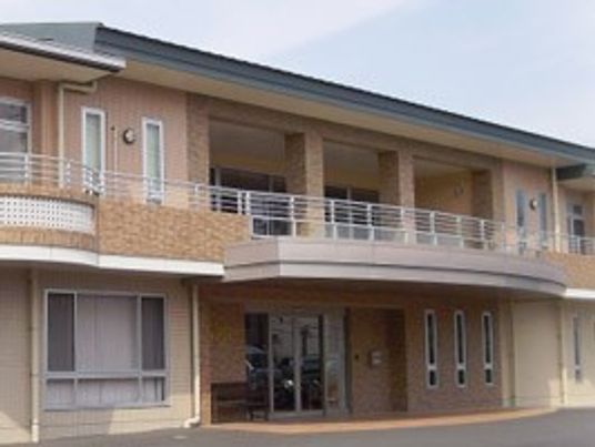 ２階建ての建物はブラウン系で、玄関の上には屋根、２階にはベランダがある。