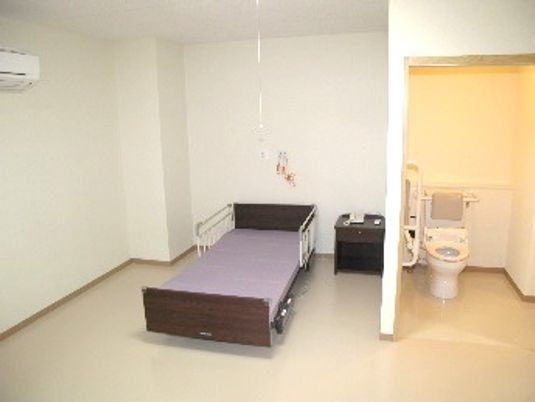 部屋の中にベッド、エアコン、トイレがある様子。緊急コールが付いている