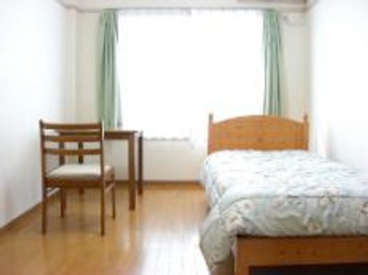 右側にベッド、左側に椅子と机が置いてある小さな部屋の様子。窓があるワンルームタイプの部屋
