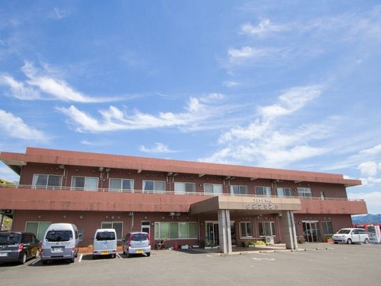 2階建ての建物。ブラウン系でベランダや車寄せが付き、敷地内には駐車場もある。