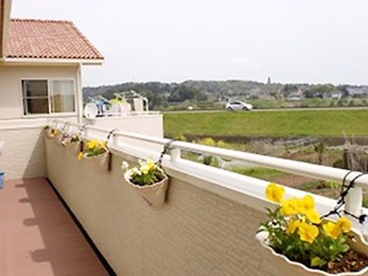 黄色のパンジーが植えられたプランターが飾られたベランダ。周囲には緑も多い。