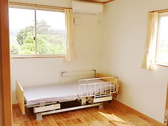 窓が二つ付いた居室には寝具付きのベッドが置かれ、温かみのあるフローリングの床。