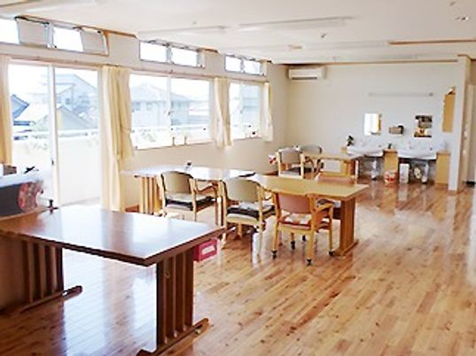 木製のダイニングテーブルが複数置かれ、洗面所も奥にあり、明るい雰囲気。