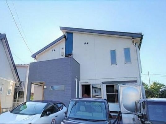 白とグレーの２階建ての建物の前には駐車場があり、車が数台止められている。