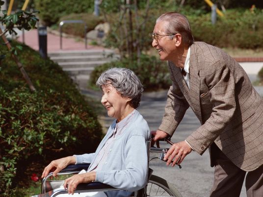 車いすに乗った女性とそれを押す男性。公園のようなのどかな場所