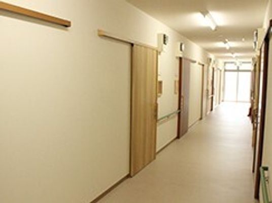 幅の広い廊下の両サイドに手すりと居室のドアがあり、突き当たりには大きな窓がある。