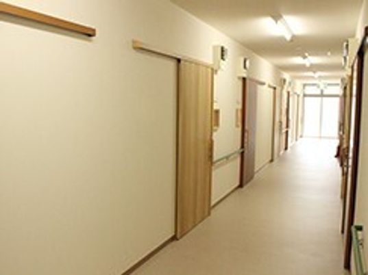 幅の広い廊下の両サイドに手すりと居室のドアがあり、突き当たりには大きな窓がある。
