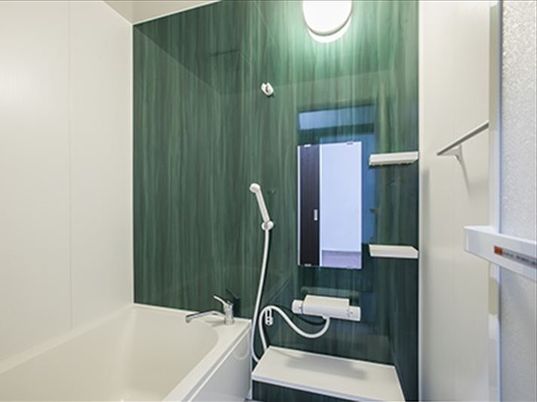 シャワーの設置された壁がグリーン、それ以外は白でまとめられた浴室。一般家庭と同じようなサイズ。