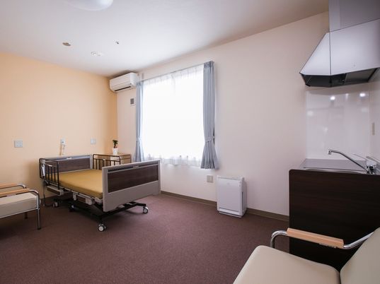 広い居室には介護用のベッドやいすが置かれ、本格的なキッチンやエアコンも完備されている。