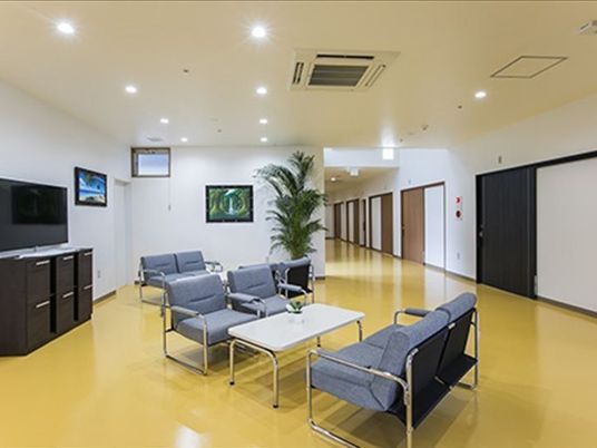 広い廊下の一角にある談話スペース。グレーのいすと白いテーブルのセットやテレビが置かれている。