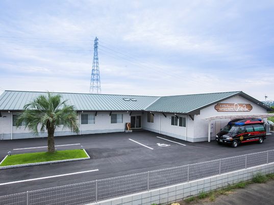 平屋建ての建物はエル字型で駐車場スペースもある。白い外壁にホームの名前が書かれている。