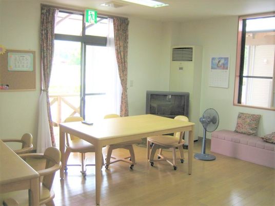 リビングダイニングはゆったりとした造りでテレビや木製のダイニングテーブルが複数置かれ、扇風機やベンチも設置されている。