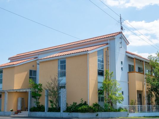 オレンジの瓦屋根が付いたオレンジの2階建ての建物。中庭があり、建物周りにも木が植えられている。