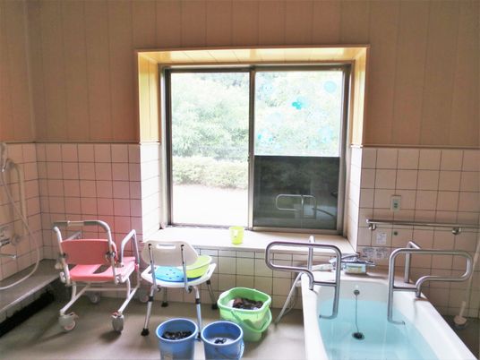 大きな窓が付いた浴室にはシャワーチェアや個浴、洗い物が入ったバケツが置かれている。