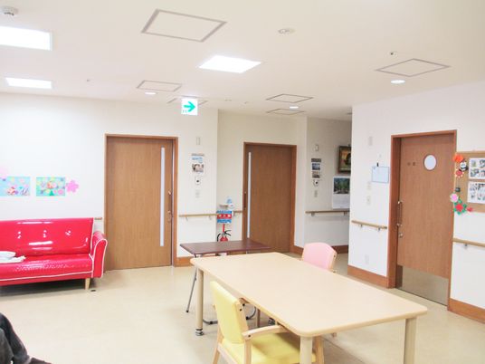 赤いソファや木製のダイニングテーブルなどが置かれた共有スペースの壁には手すりが設置され、入居者の作品も飾られている。