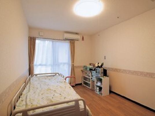 寝具付きのベッドや収納ケース、エアコンが設置されたフローリングの部屋には大きな窓が付いている。