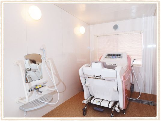 車いすに座ったまま入浴できる機械浴が設置された白を基調とした浴室。シャワースペースもある。