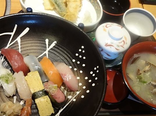 黒いさらにお寿司が並んでいる様子。吸い物や天ぷら、茶わん蒸しも写っている