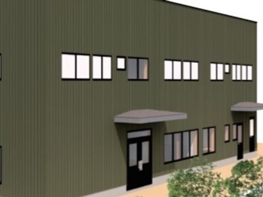 ブラウン系の2階建ての建物の外壁で、出入り口には屋根が付き、周りには草木が植えられている。