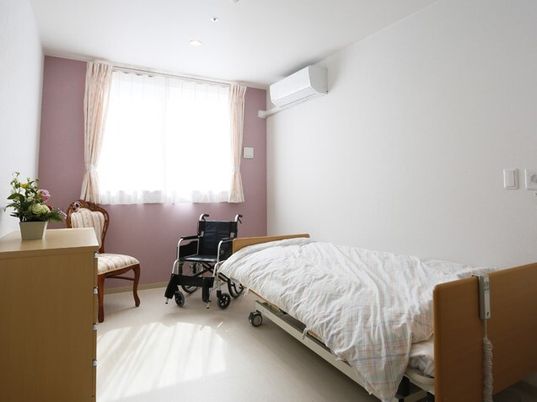 大きな窓が付いた部屋にはエアコンや寝具付きのベッド、タンスなどがあり、花も飾られている。