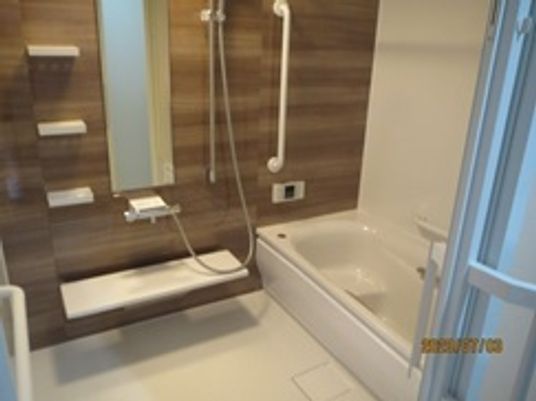白とブラウンの浴室には一人用の浴槽が設置され、手すりがたくさん付いている。