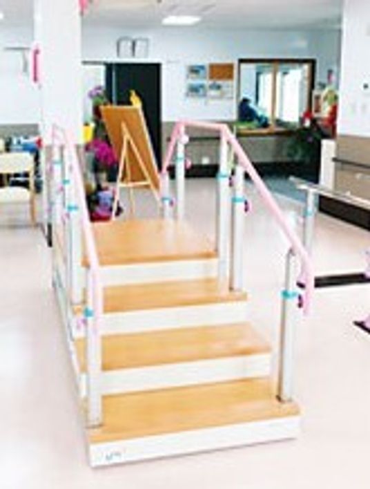 昇降台や平行棒があるリハビリスペースが手前にあり、奥にはスタッフステーションが設置されている。