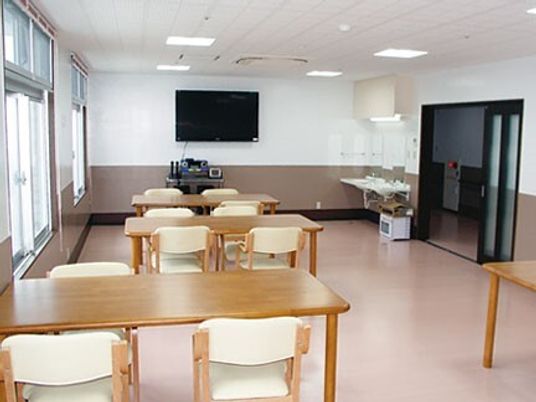 木製のダイニングテーブルセットが複数置かれている食堂には大きなテレビがあり、車いす対応の洗面所もある。