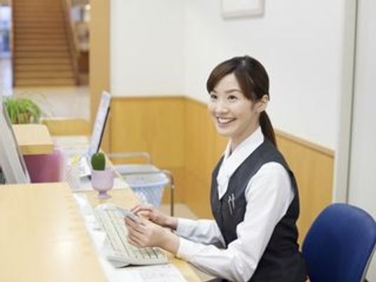 受付にて椅子に座ってパソコンを使いながら業務を行ってる女性スタッフ。
