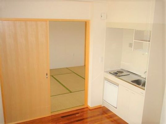 IHクッキングヒーター付きのキッチンは白く、ミニ冷蔵庫も付いている。畳敷きの部屋には家具などはない。