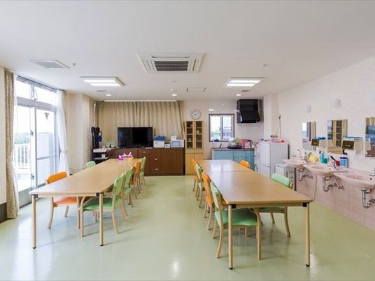 食堂には木製のテーブルが２つ並び、奥にはテレビも置かれている。窓が大きく日当たり良好。