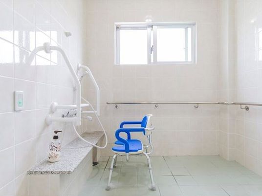 白を基調とした浴室はシンプルで清潔感がある。シャワーの前にシャワーチェアが設置されている。