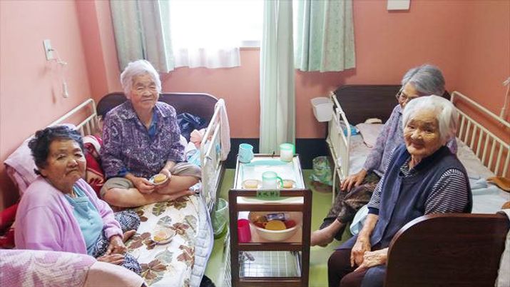 二つ並んだベッドに座って談笑している4人の女性入居者。