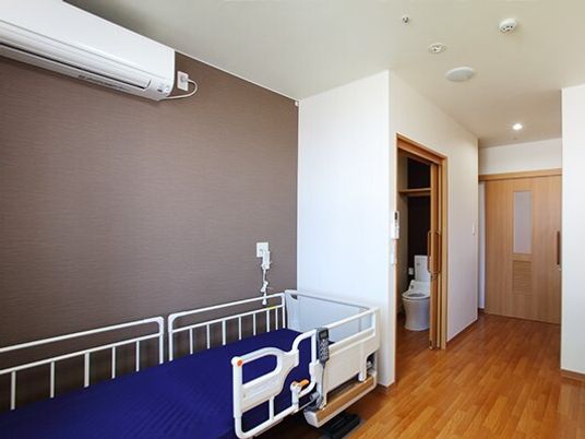 エアコンや介護用ベッドが置かれたフローリングの居室にはトイレや引き戸が付いている。
