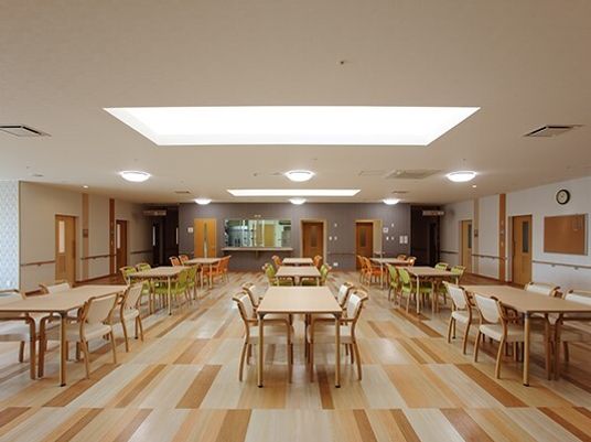 木製のダイニングテーブルが並び、いすがセットされた食堂。明るい雰囲気で奥に厨房もある。