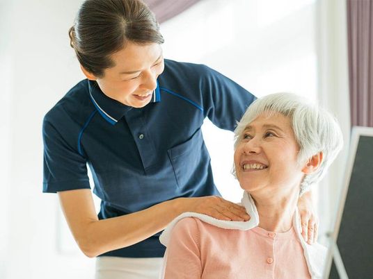 高齢者の方にタオルをかけてマッサージしているスタッフと振り返りながら会話する女性の様子