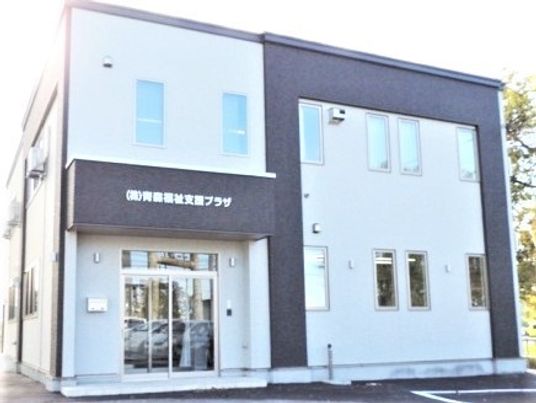 車いすに乗った眼鏡の男性入居者と屋外での散歩を楽しむエプロン姿の女性スタッフ。