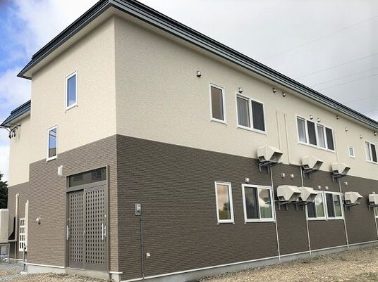 白とダークブラウンの2階建ての建物にはたくさんの窓が付き、原っぱが近くにある。