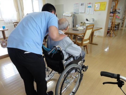 ポロシャツを着た男性スタッフが車いすの男性入居者に話しかけている様子。