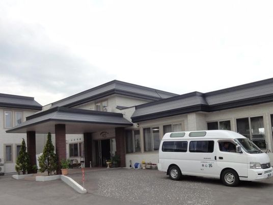2階建ての建物の前にはホームの名前が入った福祉車両がある。玄関には長い屋根が付き、雨をしのげる。