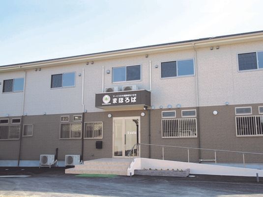 白とブラウンの2階建て。駐車場もあり、玄関にはスロープと手すり、階段が設置されている。