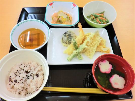 天ぷらや赤飯、吸い物、2種類の小鉢が並んだ黒いトレー。