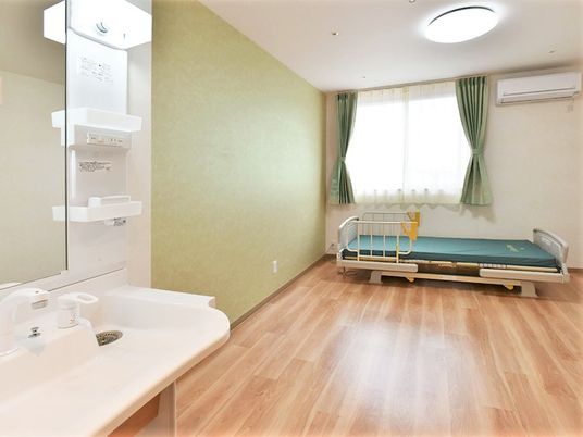 フローリングの居室。大きな窓のそばにベッドが付いたシンプルな洋風の部屋となっている。