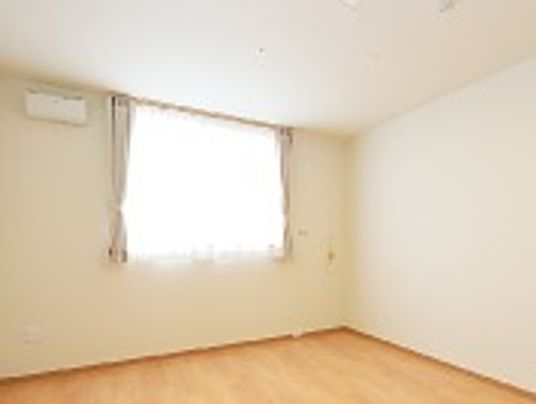 フローリングの居室。エアコンが設置され、大きな窓にはカーテンがある。