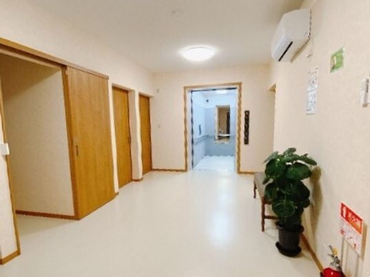 奥にエレベーターがある廊下の様子。左側に個室が並んでいる様子